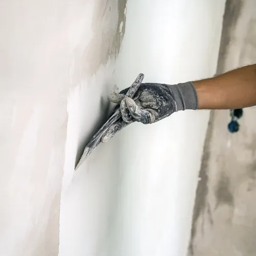 Hand with gloves smoothing a white wall using a plastering trowel.