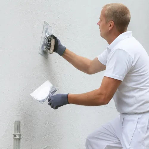 Mann in weißer Arbeitskleidung verspachtelt eine Wand mit zwei Glättkellen.
