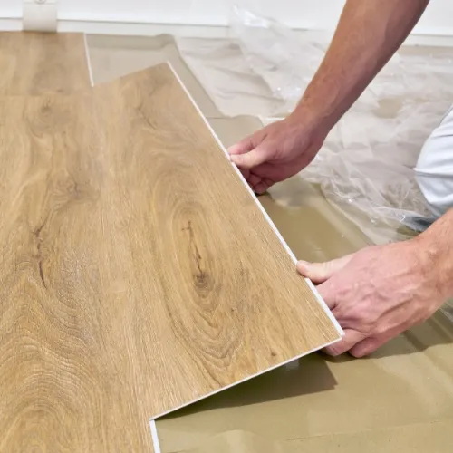Person verlegt eine Holzoptik-Vinylbodenplatte auf einem Bodenbelag.